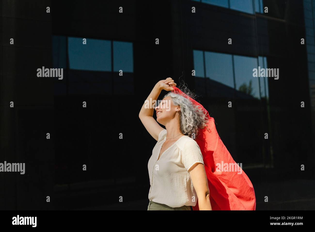 Geschäftsfrau mit rotem Blazer genießt den sonnigen Tag vor der Wand Stockfoto