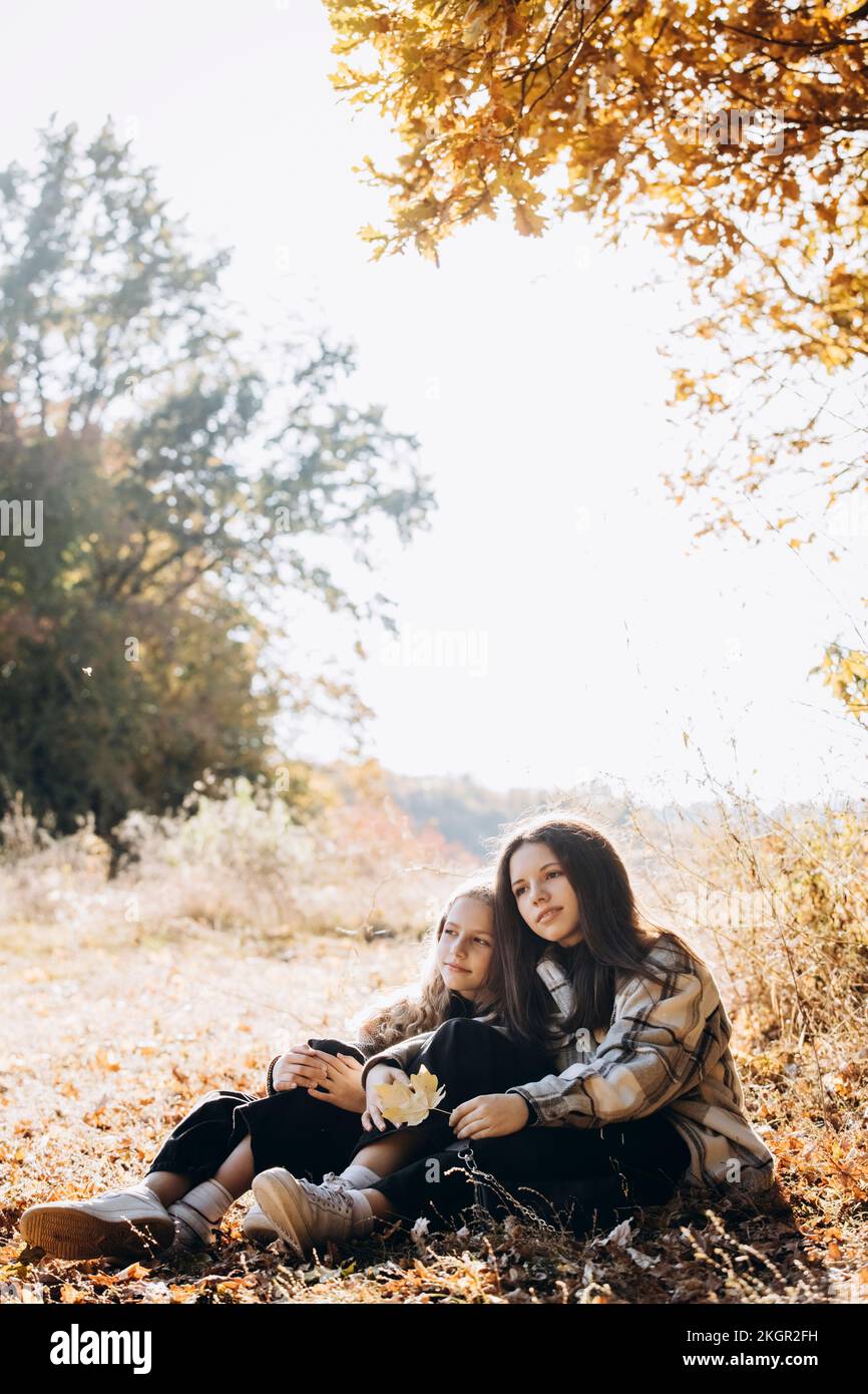 Ein Mädchen, das mit seiner Schwester im Herbstwald sitzt Stockfoto