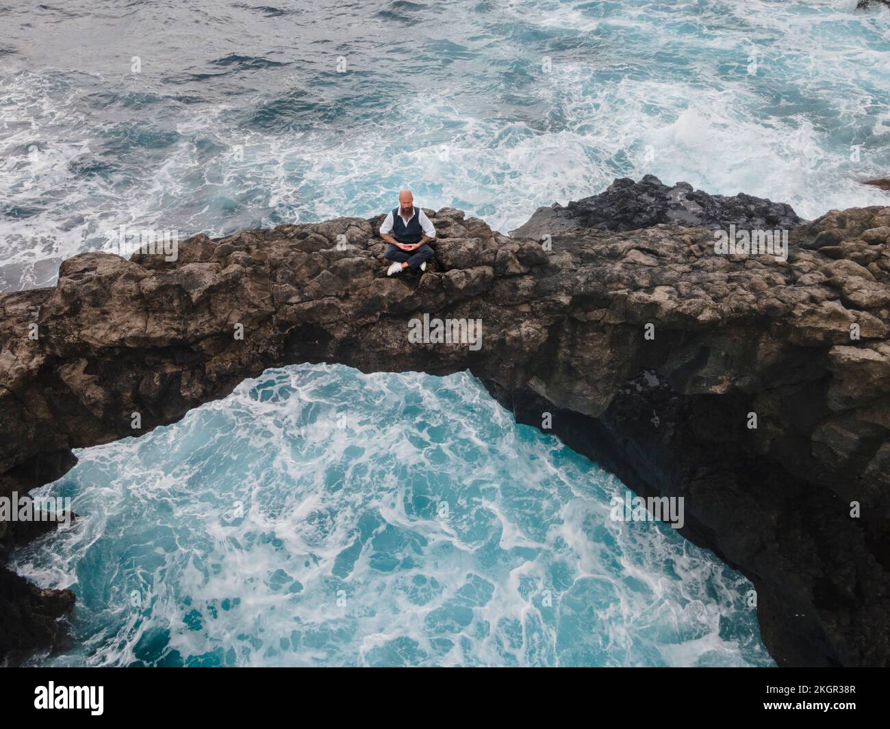 Reifer Mann, der Meditation auf einem Felsbogen über dem Meer praktiziert Stockfoto