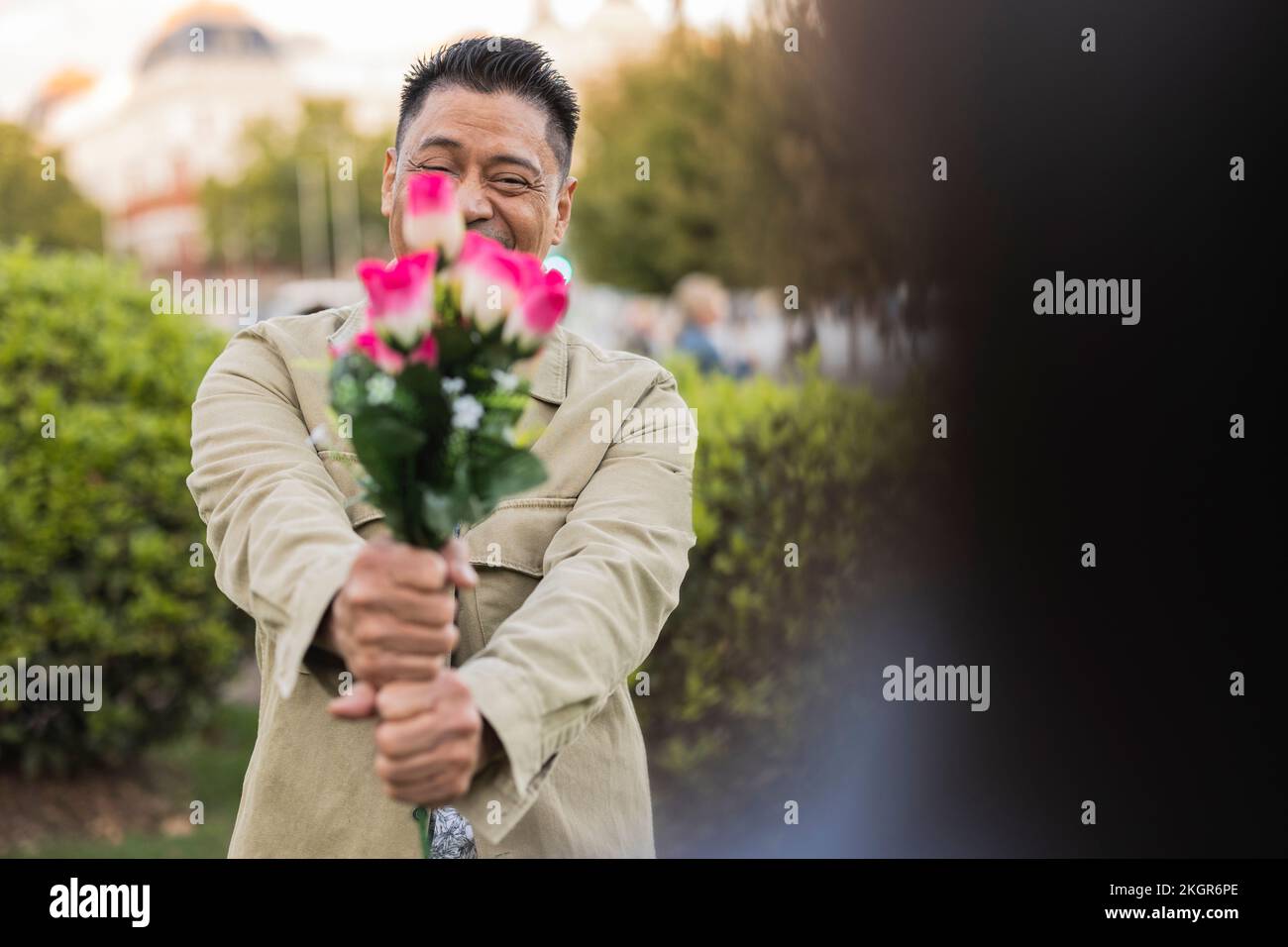 Ein lächelnder, reifer Mann, der am Valentinstag im Park Blumen zeigt Stockfoto