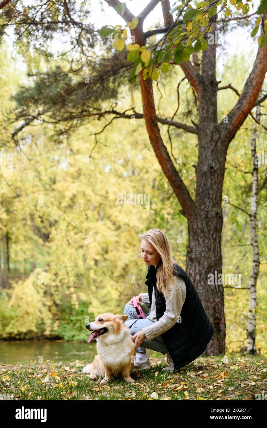 Blonde Frau streichelt süßen Hund im Herbstwald Stockfoto