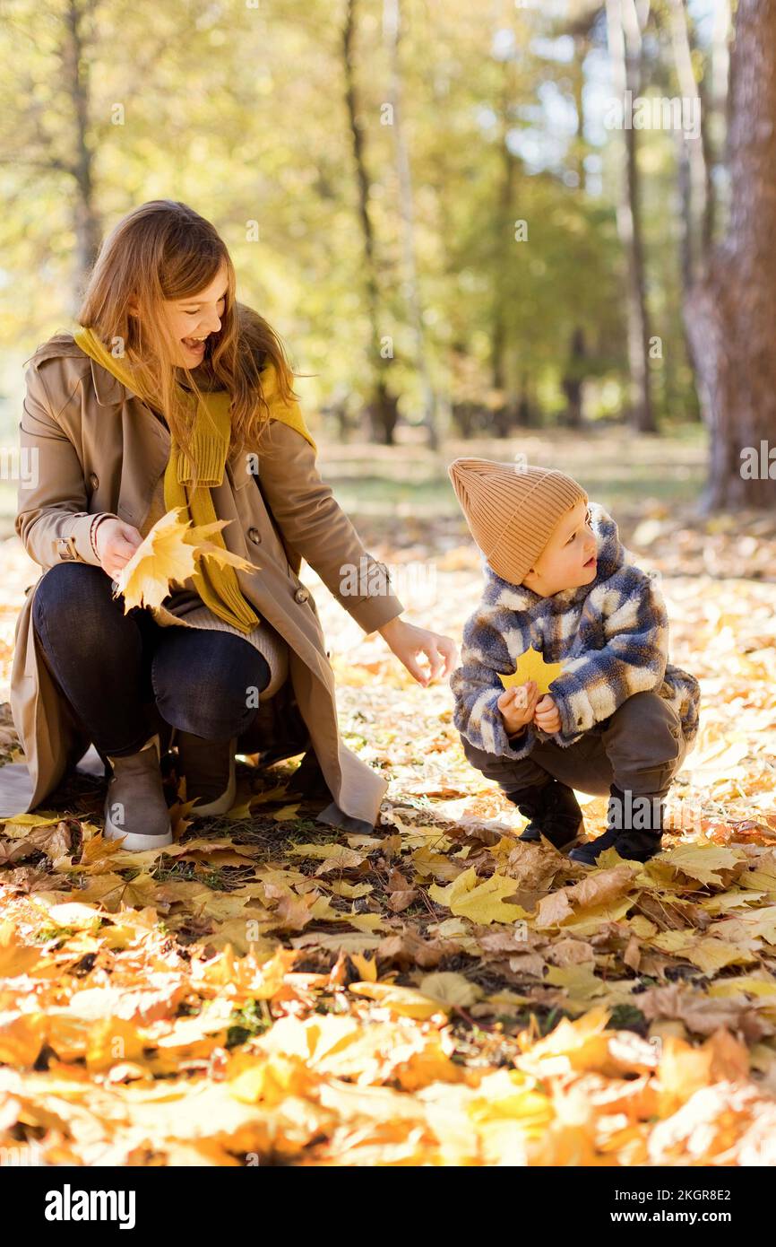 Glückliche Mutter und Sohn in der Hockposition, die gelbes Blatt im Park halten Stockfoto