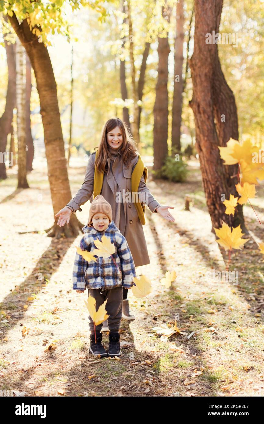 Mutter wirft Herbstblätter über den Sohn im Park Stockfoto