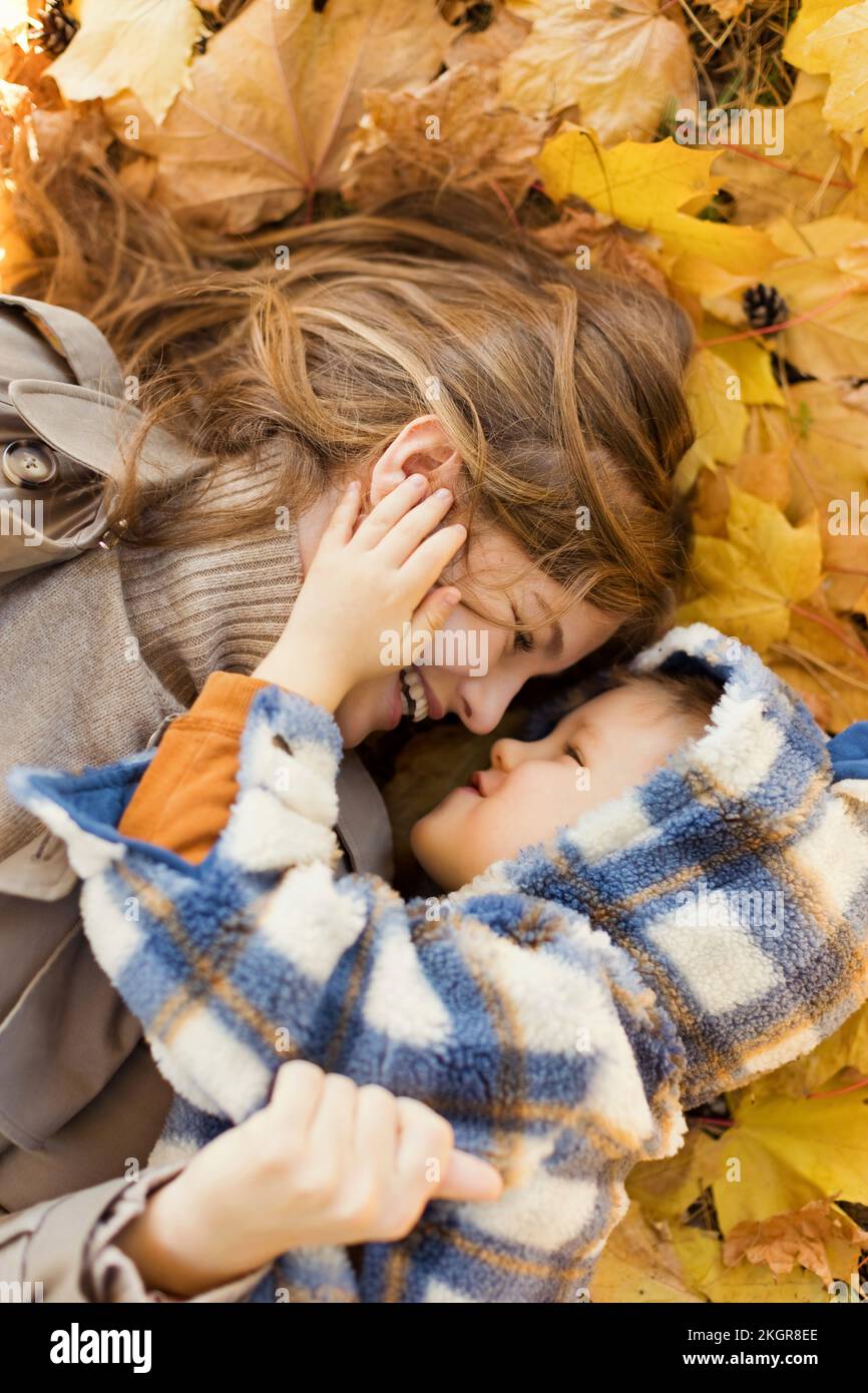 Mutter und Sohn liegen auf gelben Herbstblättern im Park Stockfoto