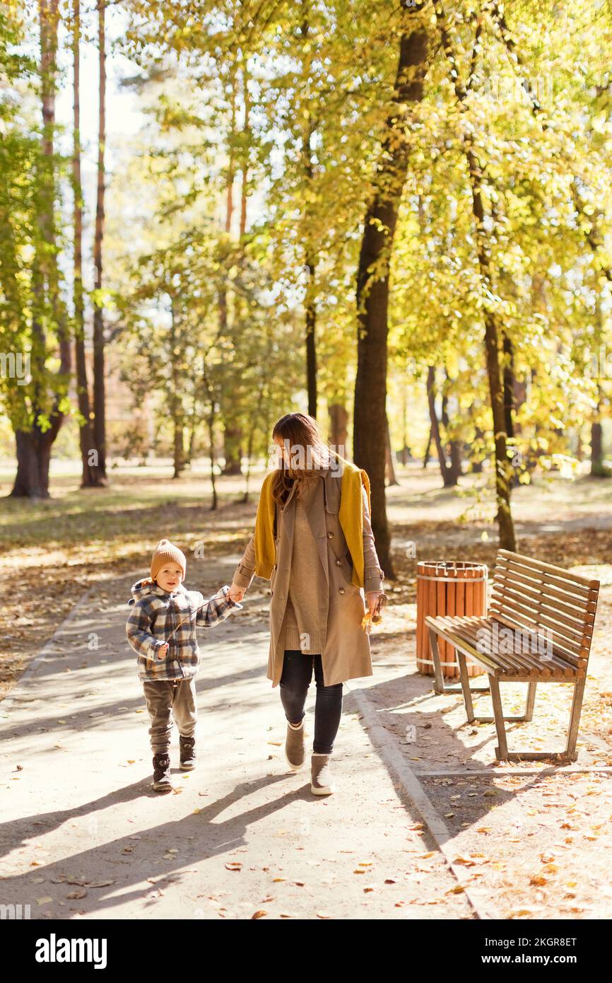 Mutter und Sohn gehen zusammen und halten Händchen auf dem Fußweg im Park Stockfoto