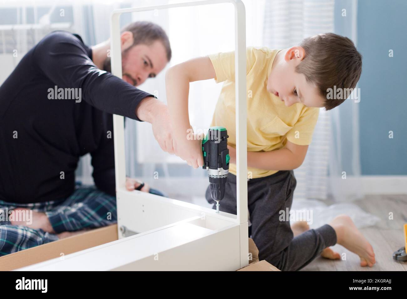 Ein Junge, der einen Power-Schraubenzieher auf dem Tisch benutzt, von seinem Vater zu Hause Stockfoto
