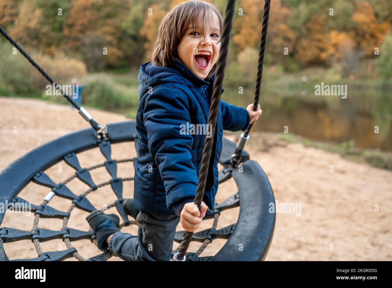 Ein fröhlicher, süßer Junge, der im Herbstpark auf einer Nestschaukel spielt Stockfoto