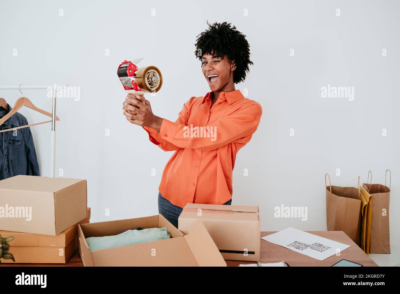 Fröhliche junge Geschäftsfrau mit Klebebandabroller, die am Schreibtisch steht Stockfoto
