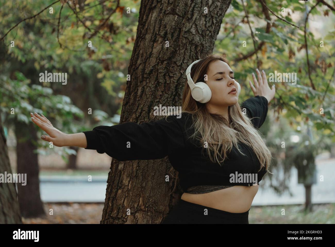 Junge Frau, die Musik über kabellose Kopfhörer hört und mit ausgestreckten Armen auf dem Baumstamm steht Stockfoto