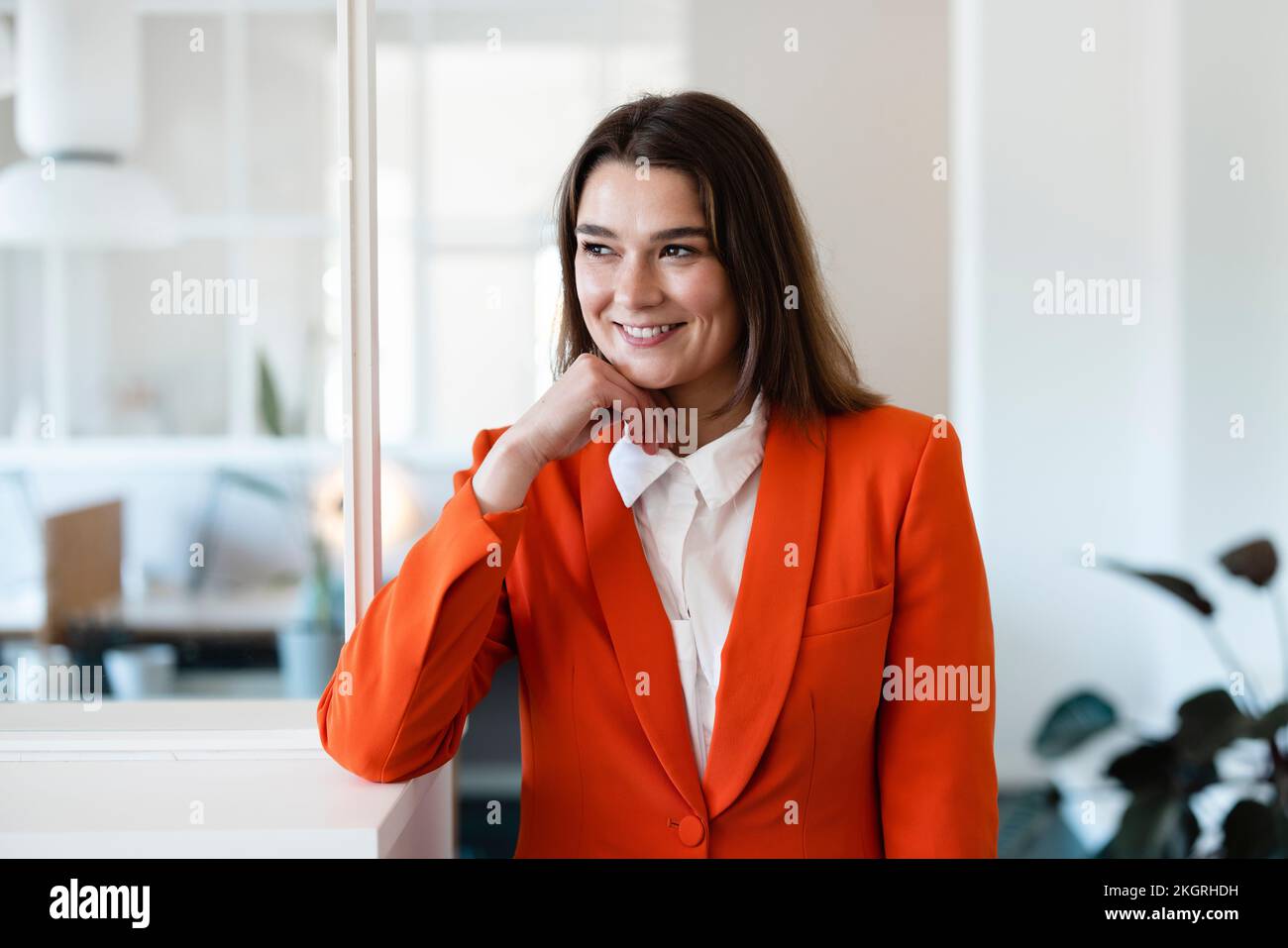 Glückliche Geschäftsfrau mit der Hand am Kinn im Büro Stockfoto