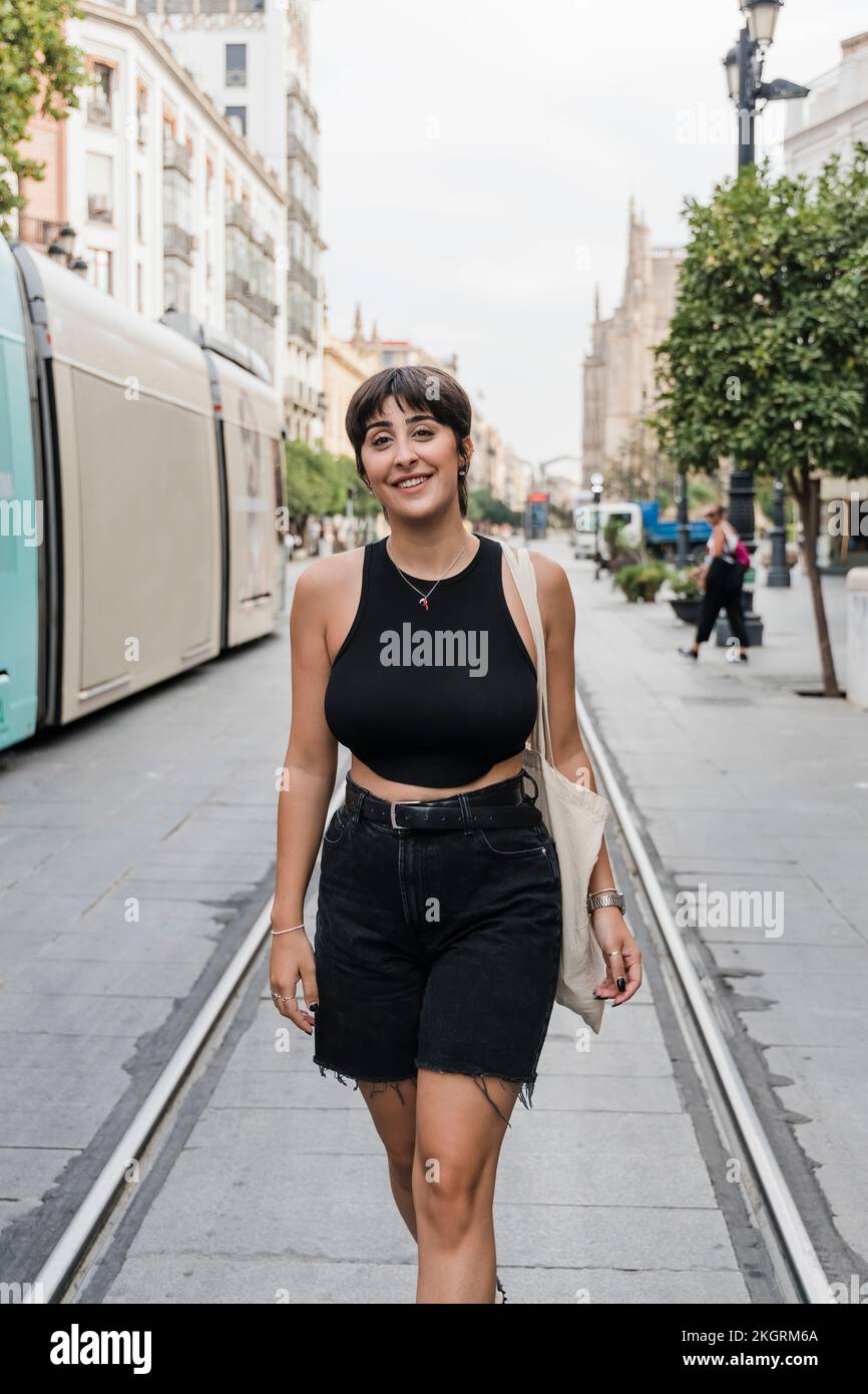 Lächelnde junge Frau mit kurzen Haaren, die in der Straßenbahn auf der Straße spaziert Stockfoto