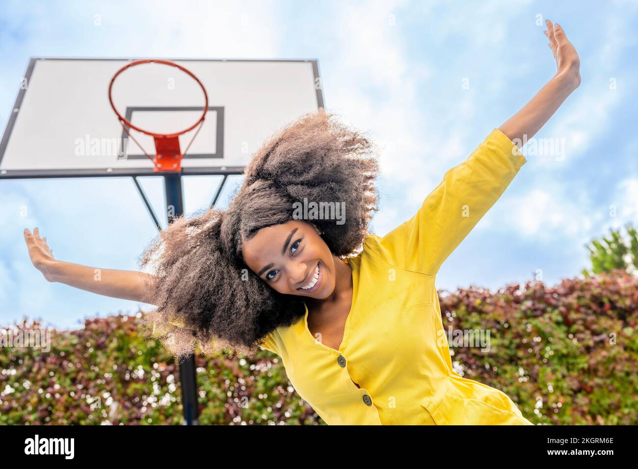 Eine sorgenfreie junge Frau mit ausgestreckten Armen, die vor dem Basketballkorb steht Stockfoto