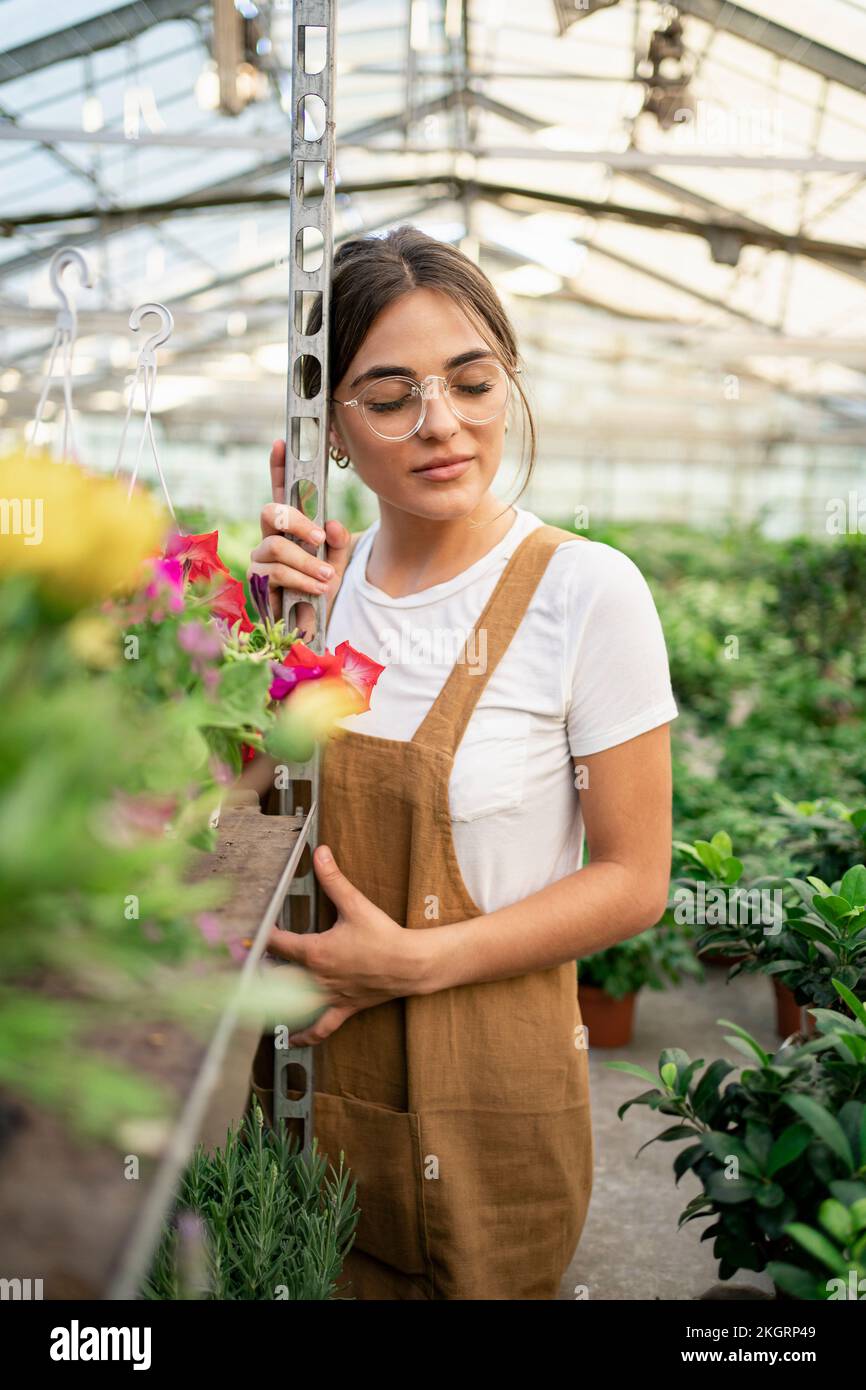 Gärtner mit geschlossenen Augen, der sich im Gewächshaus auf ein Regal lehnt Stockfoto