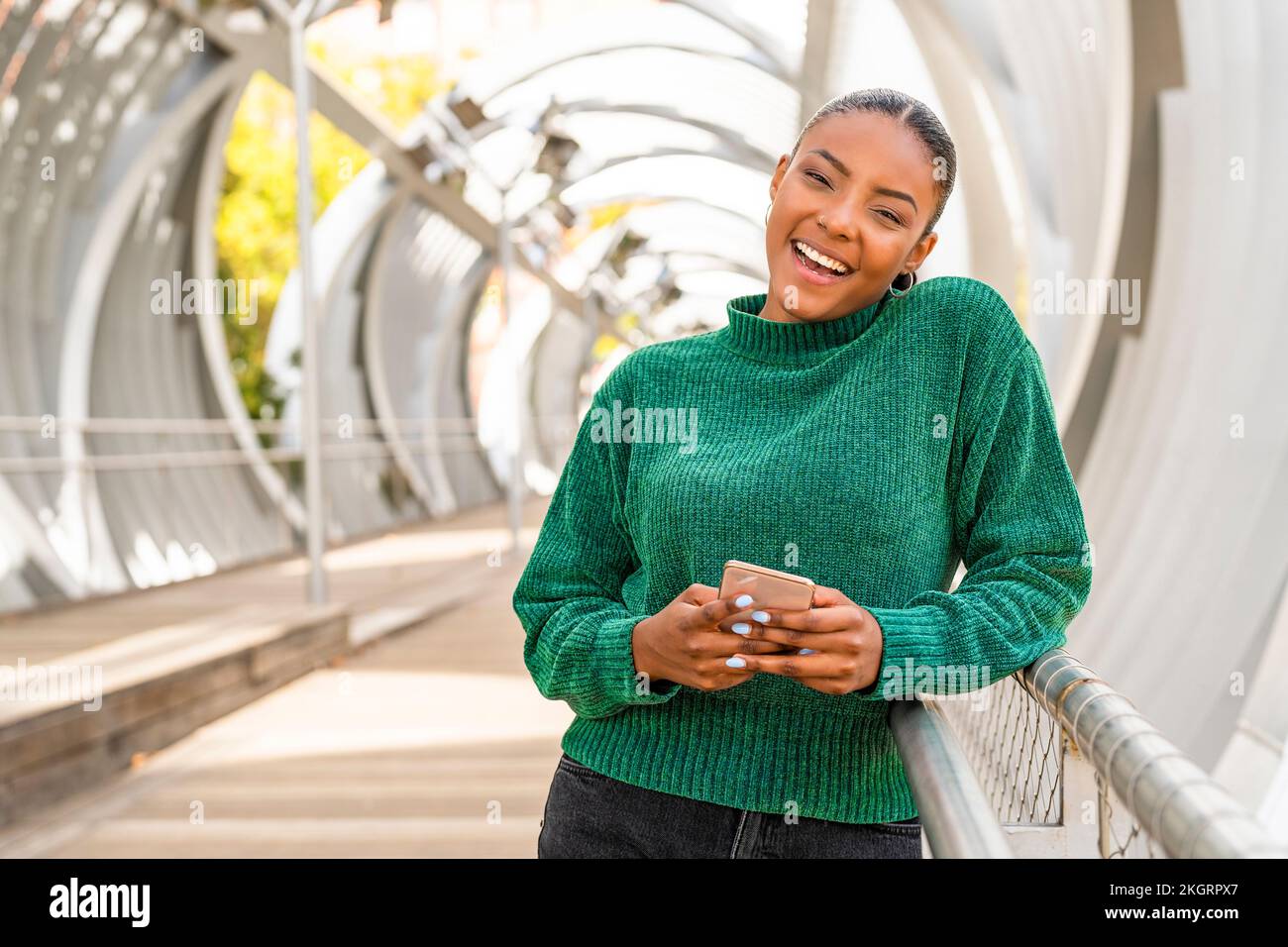 Glückliche junge Frau, die das Handy auf der Brücke hält Stockfoto