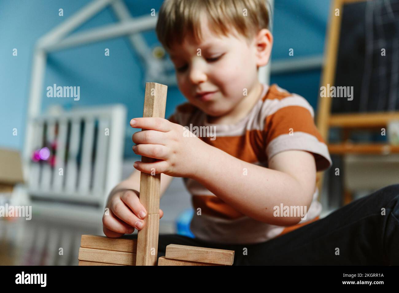 Lächelnder Junge, der zu Hause mit einem Holzblock im Schlafzimmer spielt Stockfoto