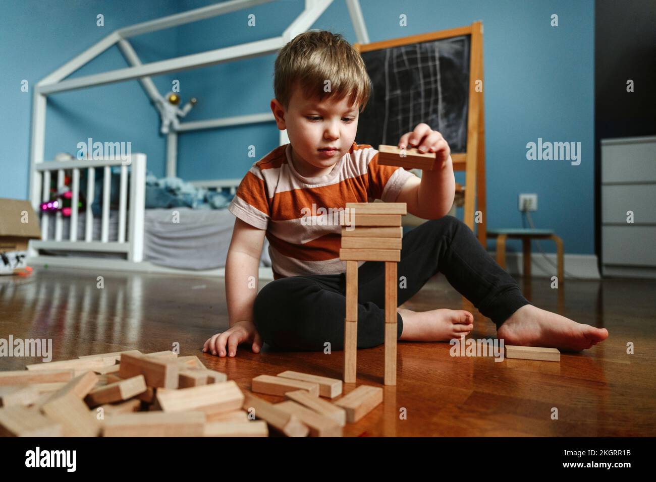 Ein Junge, der zu Hause mit einem Holzblock im Schlafzimmer spielt Stockfoto