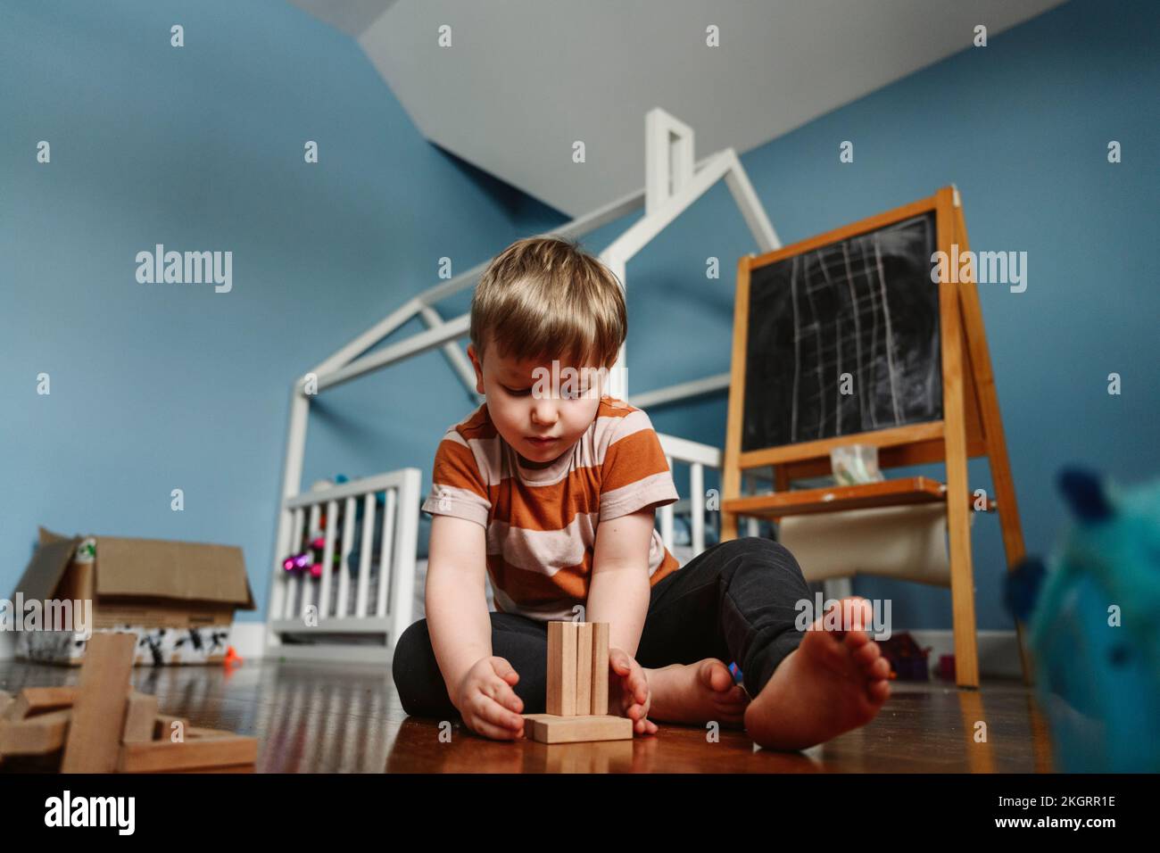 Ein verspielter Junge, der zu Hause mit einem Holzblock im Schlafzimmer spielt Stockfoto