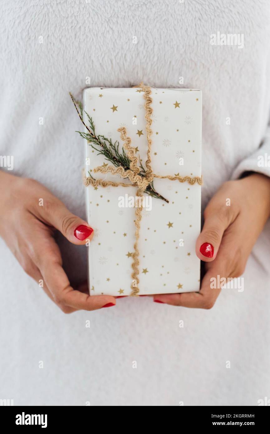 Hände einer Frau mit einem Weihnachtsgeschenk, verpackt in weißes Papier Stockfoto
