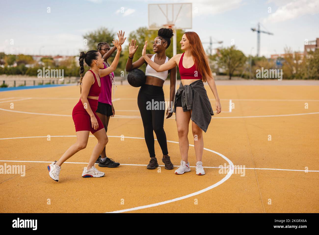 Fröhliche junge Freunde, die High-Five auf dem Basketballplatz machen Stockfoto