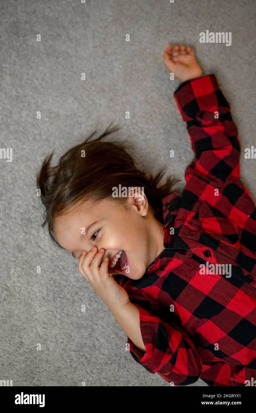 Ein glücklicher Junge mit kariertem Hemd, der auf dem Teppich lag Stockfoto