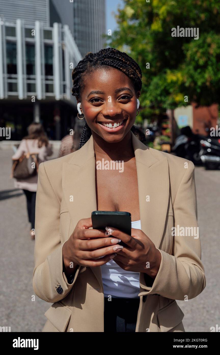 Glückliche Geschäftsfrau steht mit Smartphone auf dem Fußweg Stockfoto
