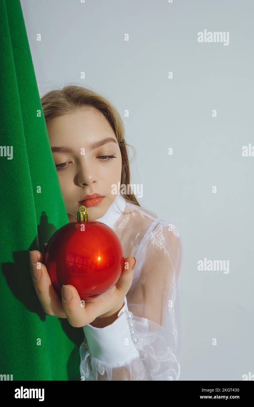 Ein Mädchen sieht sich rote Weihnachtsschmuck vor weißem Hintergrund an Stockfoto