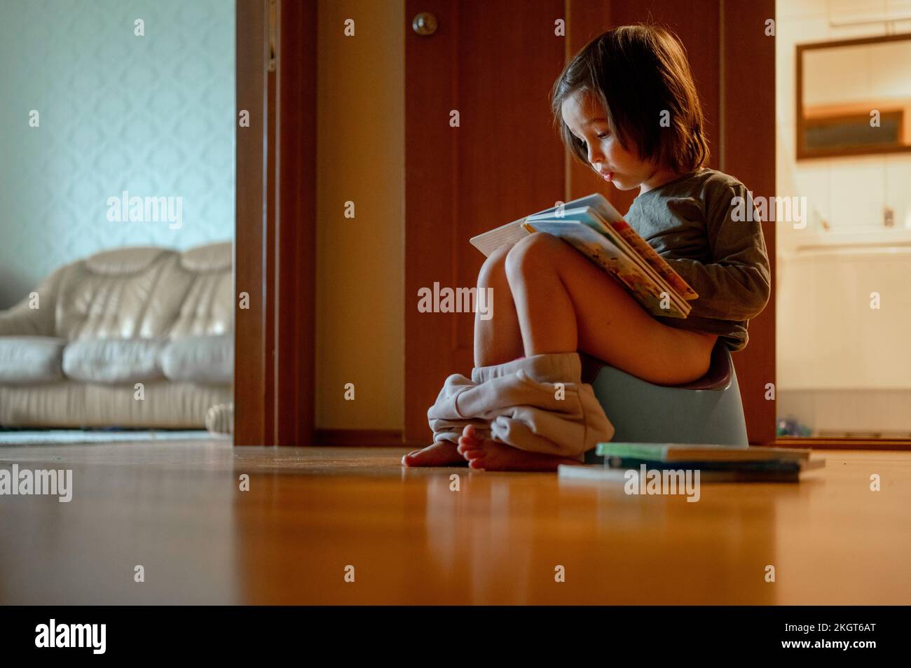 Der Junge sitzt auf dem Töpfchen und liest zu Hause ein Buch Stockfoto