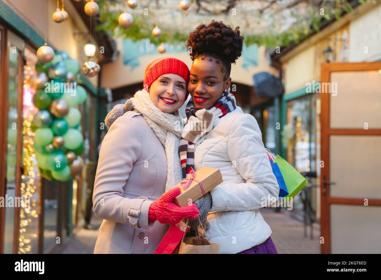 Lächelnde Frauen, die warme Kleidung tragen und Geschenke beim Weihnachtsfest halten Stockfoto