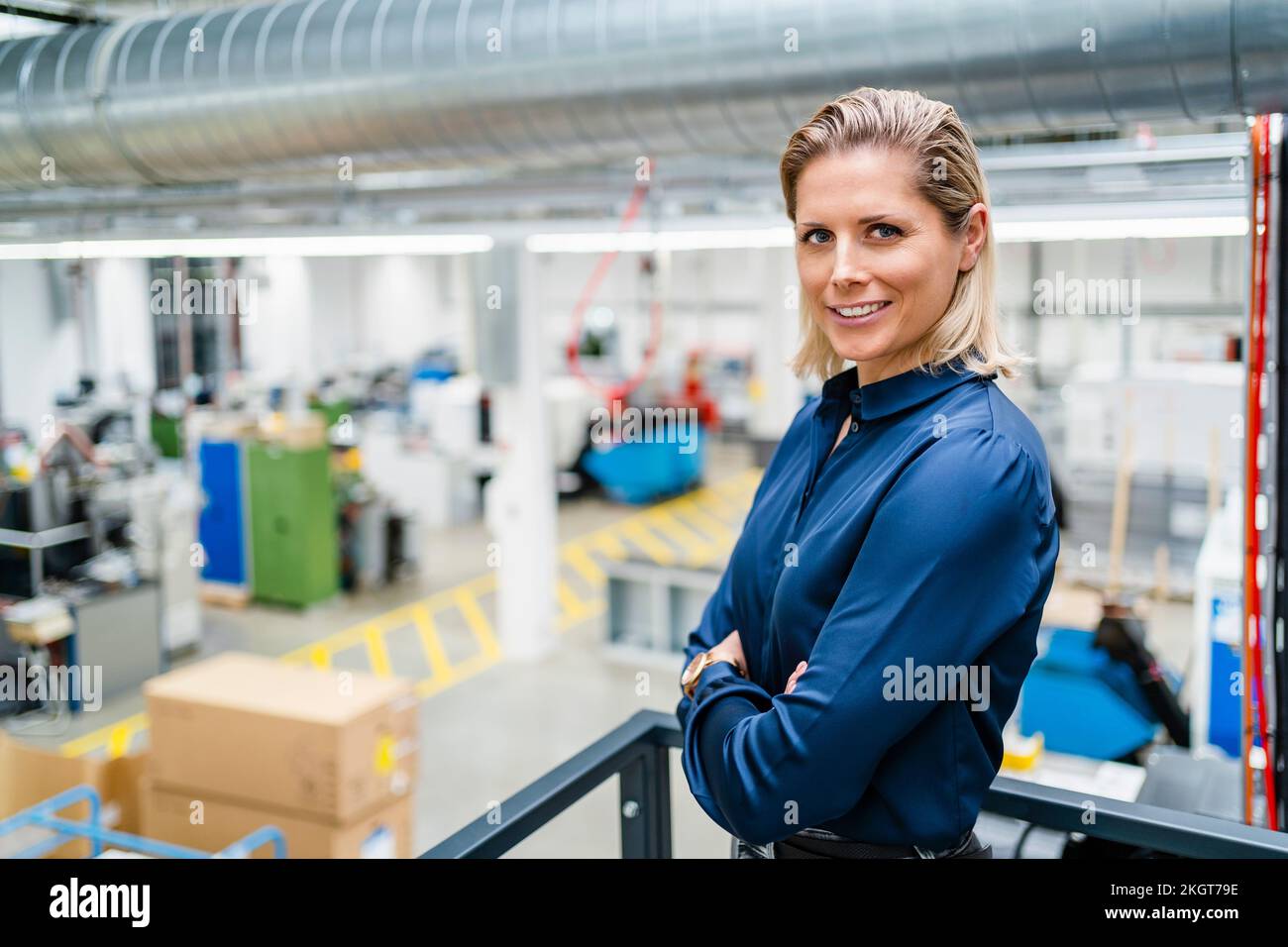 Eine selbstbewusste Geschäftsfrau, die in der Fabrik ein blaues Hemd trägt und mit gekreuzten Armen steht Stockfoto