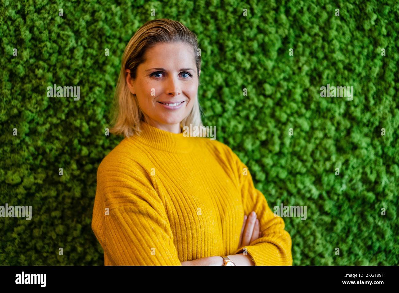 Lächelnde Geschäftsfrau mit gelbem Pullover vor der grünen Wand Stockfoto