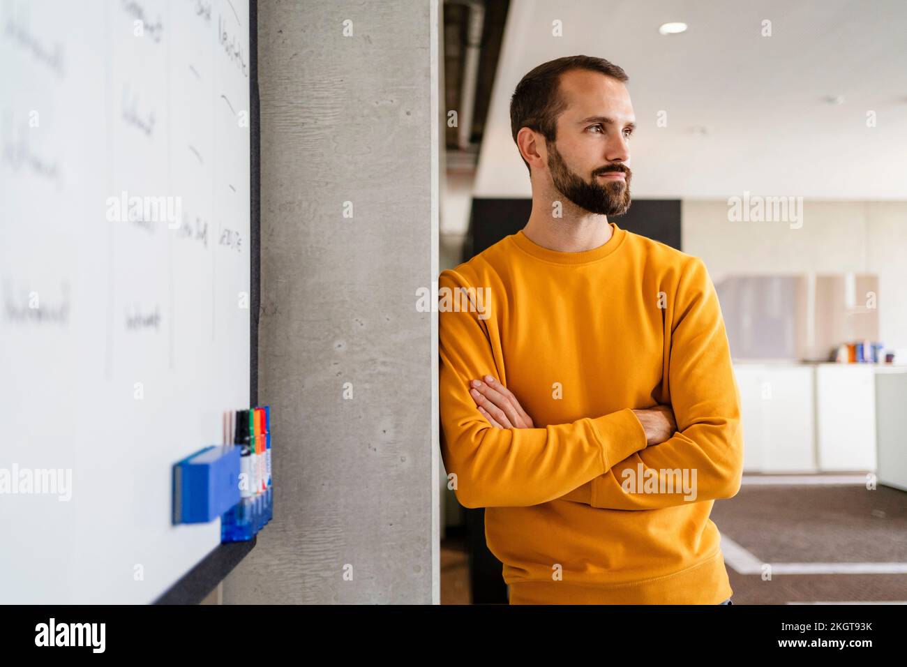 Nachdenklicher Geschäftsmann, der sich am Arbeitsplatz mit überkreuzten Armen an der Wand lehnt Stockfoto