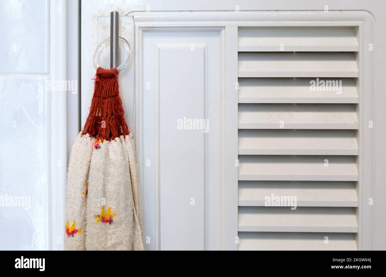 Die Nahaufnahme des Stoffhandtuchs hängt in der Nähe der weißen Tür des Schranks in der Küche, Vorderansicht mit dem Kopierraum. Stockfoto