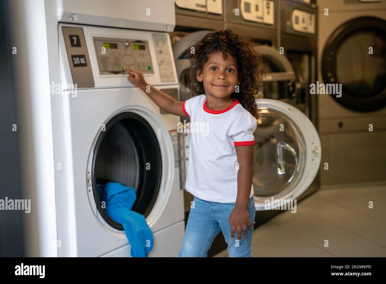 Zufriedenes Kind, das in einem Waschsalon mit Selbstbedienung für die Kamera posiert Stockfoto