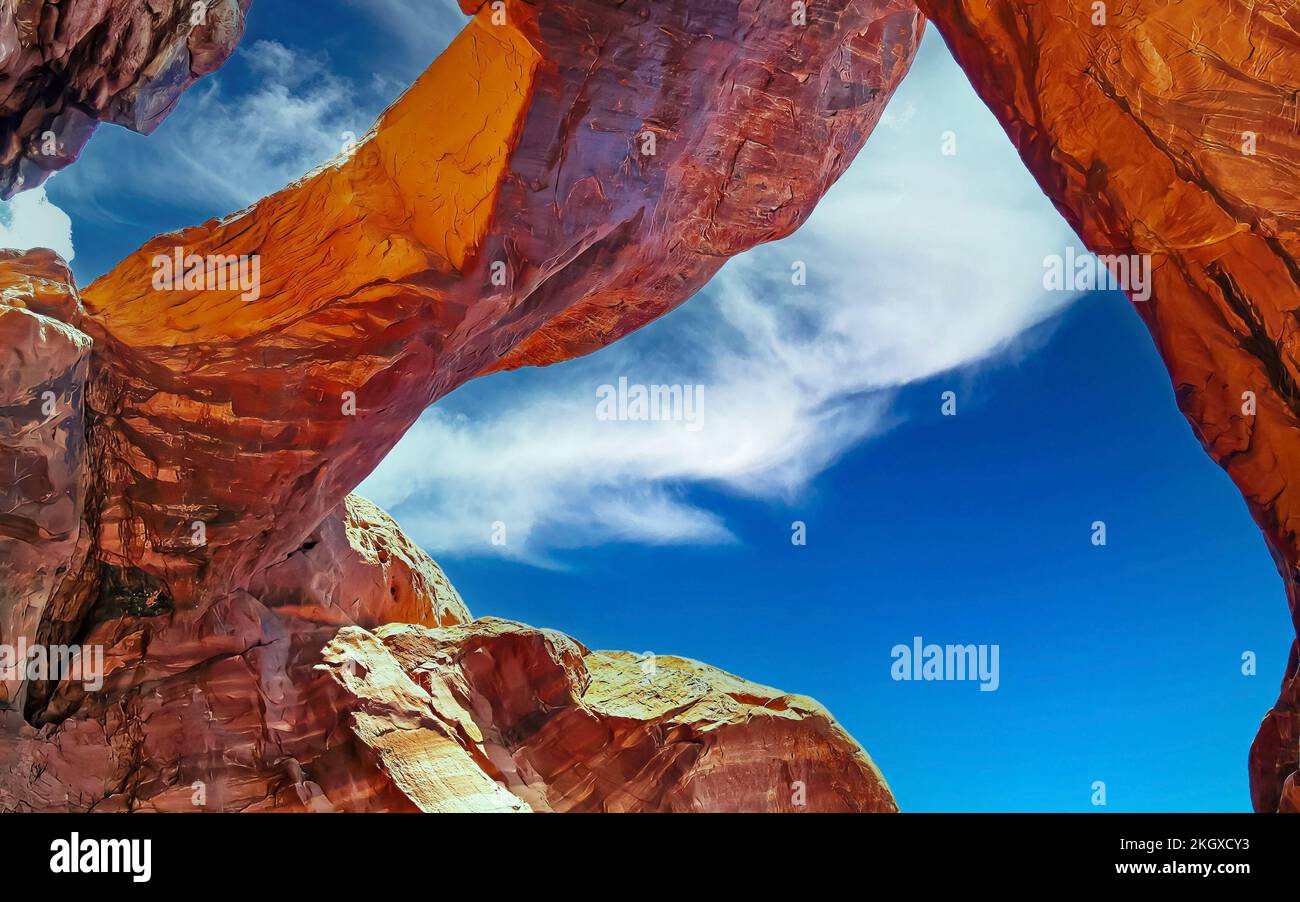 Niedriger Winkel Blick auf roten Sandsteinbrückenbogen vor blauem Himmel, flauschige Sommerwolken - Double Arch, Arches Nationalpark, Utah Stockfoto