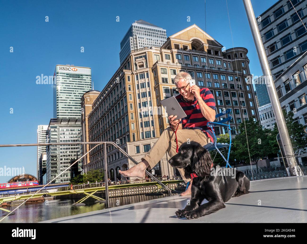 Kleiner/großer Geschäftsmann Konzept City Lage mit Hund draußen auf Bürokahn mit Smartphone iPhone & iPad Computer Canary Wharf London E14 Stockfoto