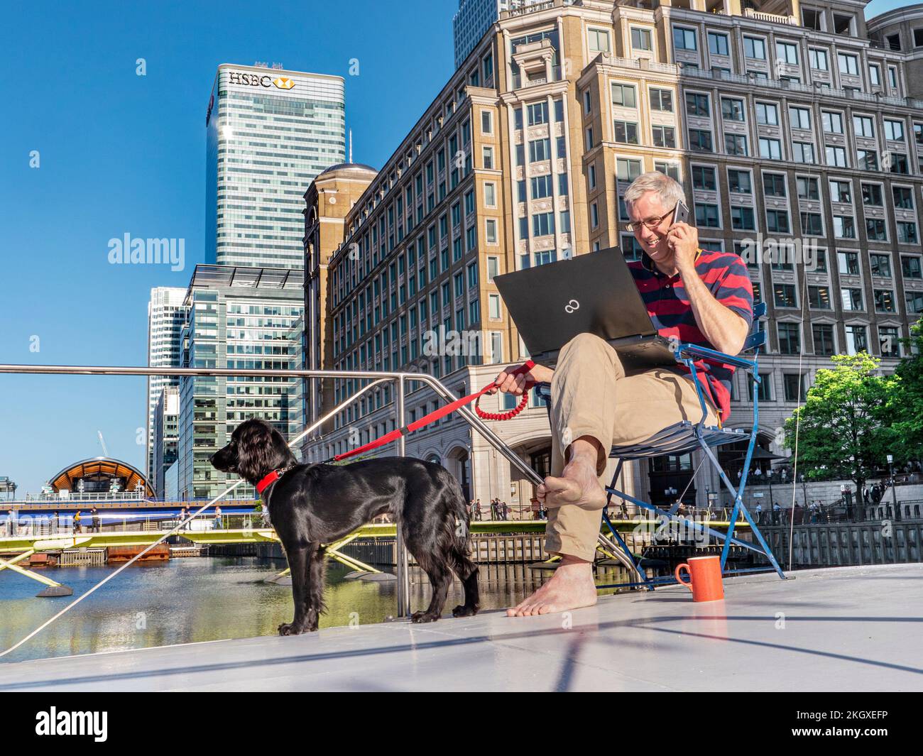 Große/kleine Unternehmen entspannte Erwachsene Männer und Hunde, die draußen auf seinem Hausboot-Barge-Büro sitzen und an seinem Laptop arbeiten Canary Wharf London E14 Stockfoto