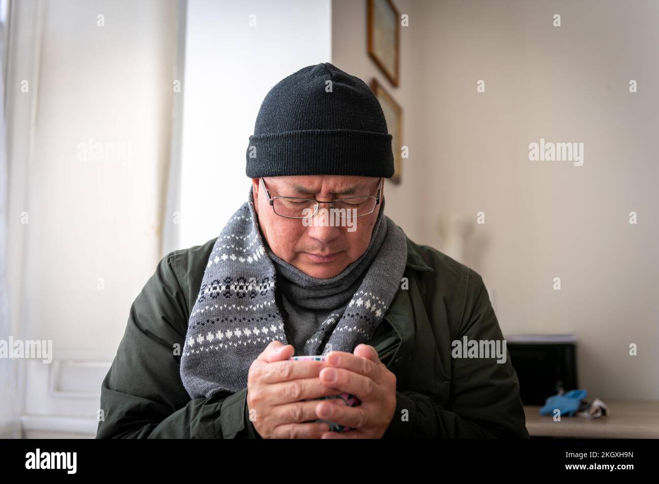 Ein älterer Mann, der versucht, sich drinnen warm zu halten, da sich die Energiekosten der Haushalte mehr als verdoppelt haben. Stockfoto