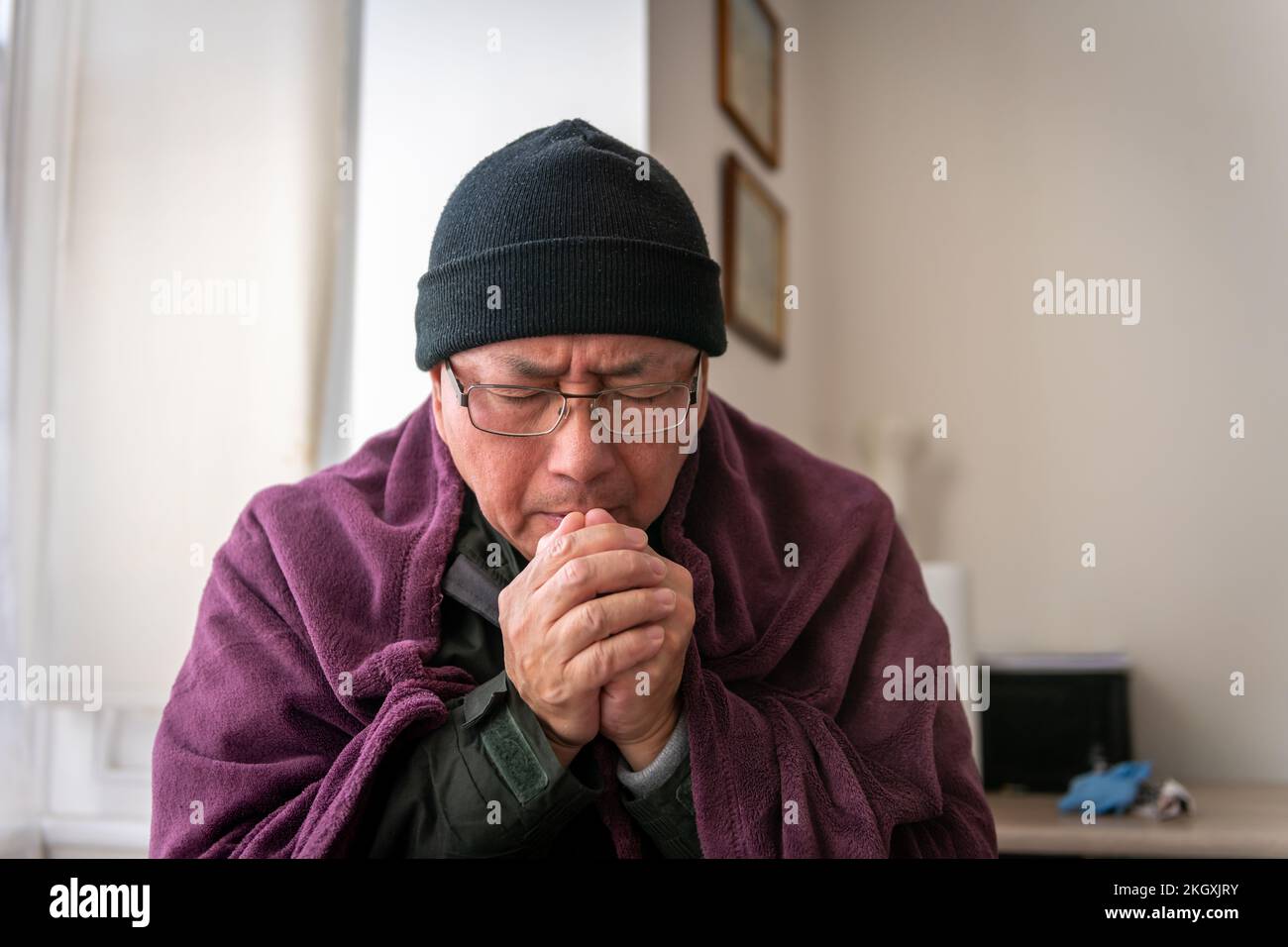 Ein älterer Mann, der versucht, sich drinnen warm zu halten, da sich die Energiekosten der Haushalte mehr als verdoppelt haben. Stockfoto