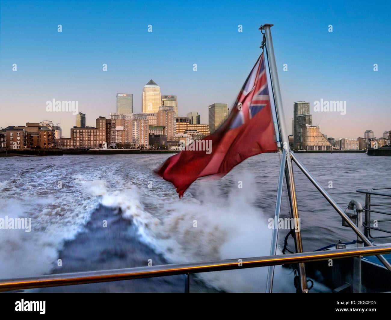 CANARY WHARF MIT ABFAHRT AUF der Themse Clipper River Boot RB1 verschwommen mit Geschwindigkeit und mit traditioneller roter Flagge von Canary Wharf am Sonnenuntergang der Themse London Großbritannien Stockfoto