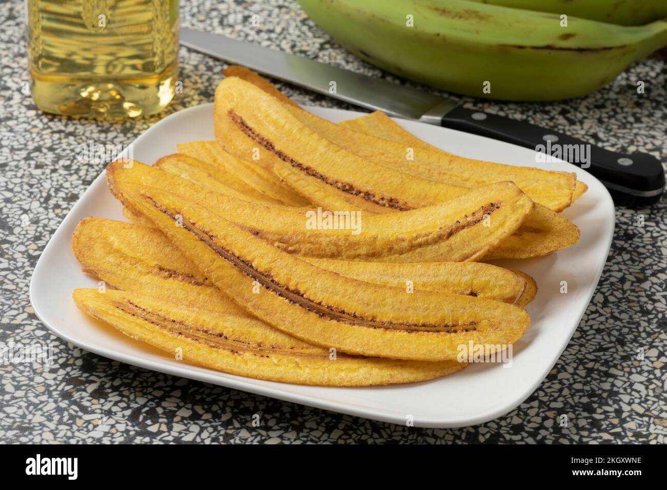 Gericht mit frisch geschnittenen und gebackenen Bananenchips aus nächster Nähe und frischen grünen Mehlbananen im Hintergrund Stockfoto