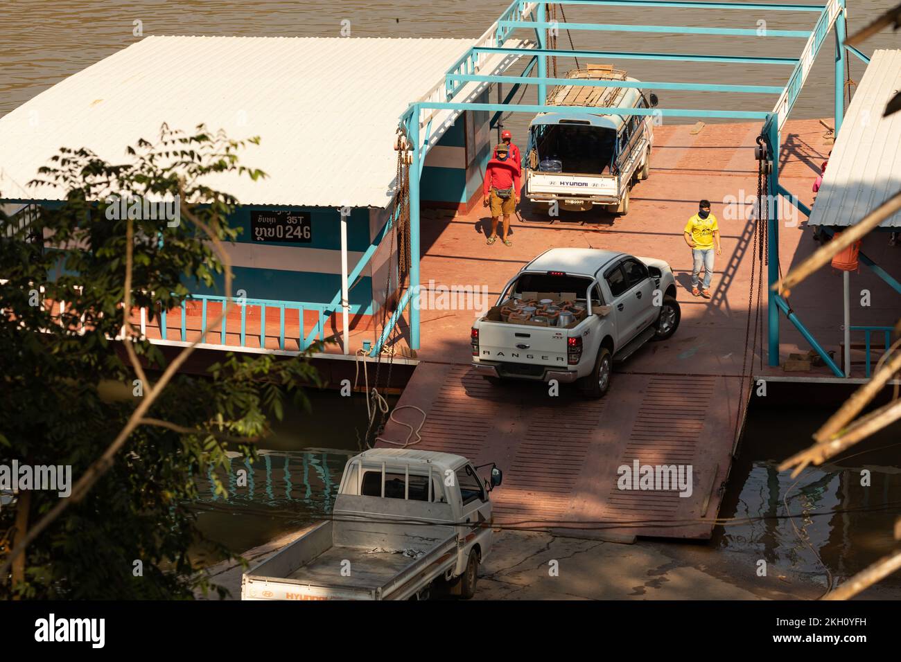 Luang Prabang, Laos - 15. Dezember 2019: Mehrere Fahrzeuge fahren auf einem der riesigen Transportschiffe auf einer Rampe am Ufer des Mekong vorbei Stockfoto
