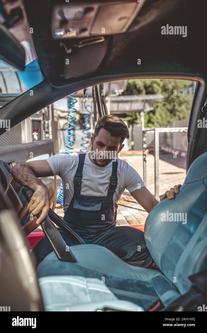 Kfz-Detaillierer, der mit dem Staubsaugen eines schmutzigen Fahrzeuginnenraums befasst ist Stockfoto