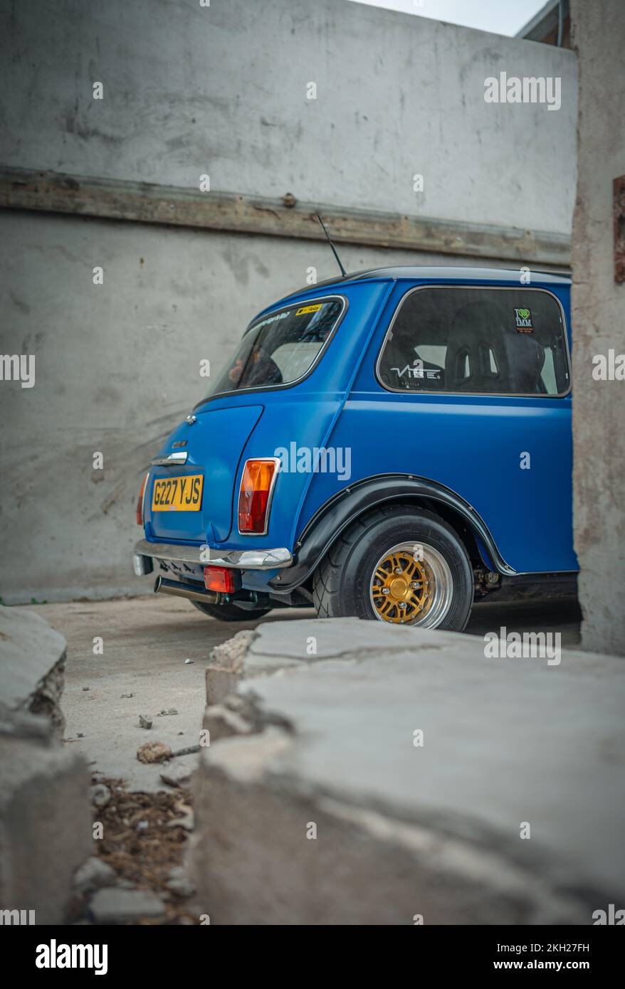 Ein vertikaler Schuss eines blauen Mini Cooper gegen eine Steinmauer nach einer langen Restaurierung Stockfoto