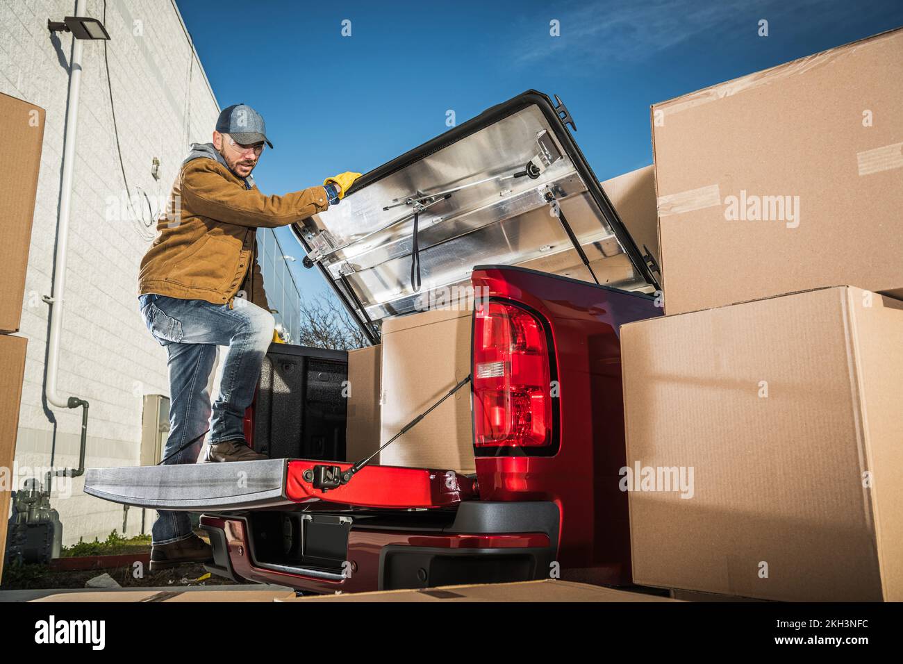 Mitarbeiter der Umzugsfirma in Kaukasien packt Kartons von Kunden in den Kofferraum seines roten Pickup-Lkws. Transportdienstleistungen. Stockfoto