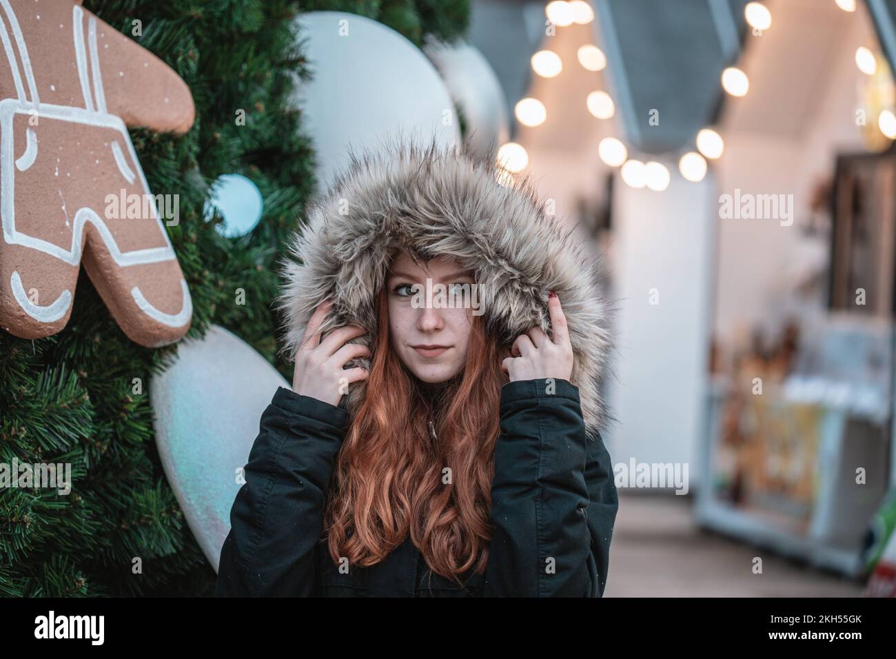 Ein Porträt eines jungen rothaarigen Mädchens in einem Pelzmantel in der Nähe des Weihnachtsbaums Stockfoto