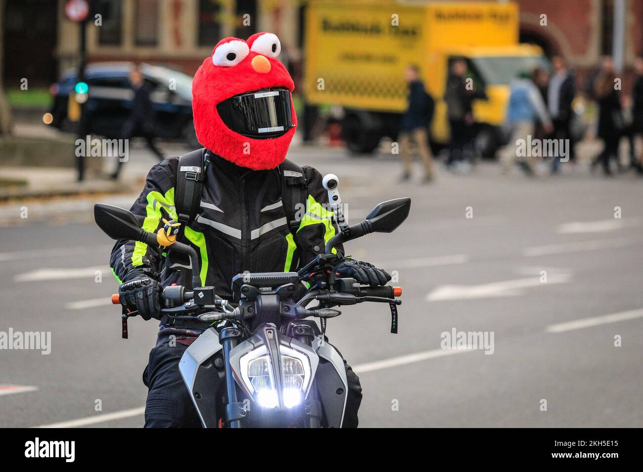 Westminster, London, Großbritannien. 23.. November 2022. Ein Biker auf  seinem Roller trägt eine helle und dennoch helmförmige Hülle in Form von  Elmo, dem pelzigen roten muppet-Monster aus der Sesamstraße, während er  heute