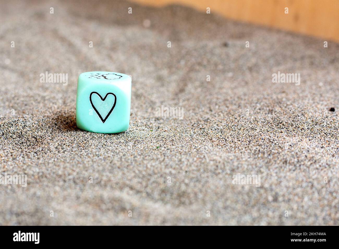 hellblauer Kunststoffwürfel mit Herz- und Wettersymbolen an den Seiten. Lustige Spielwürfel auf Sand. Valentinstag-Konzept. Liebessymbol. Schließen Stockfoto