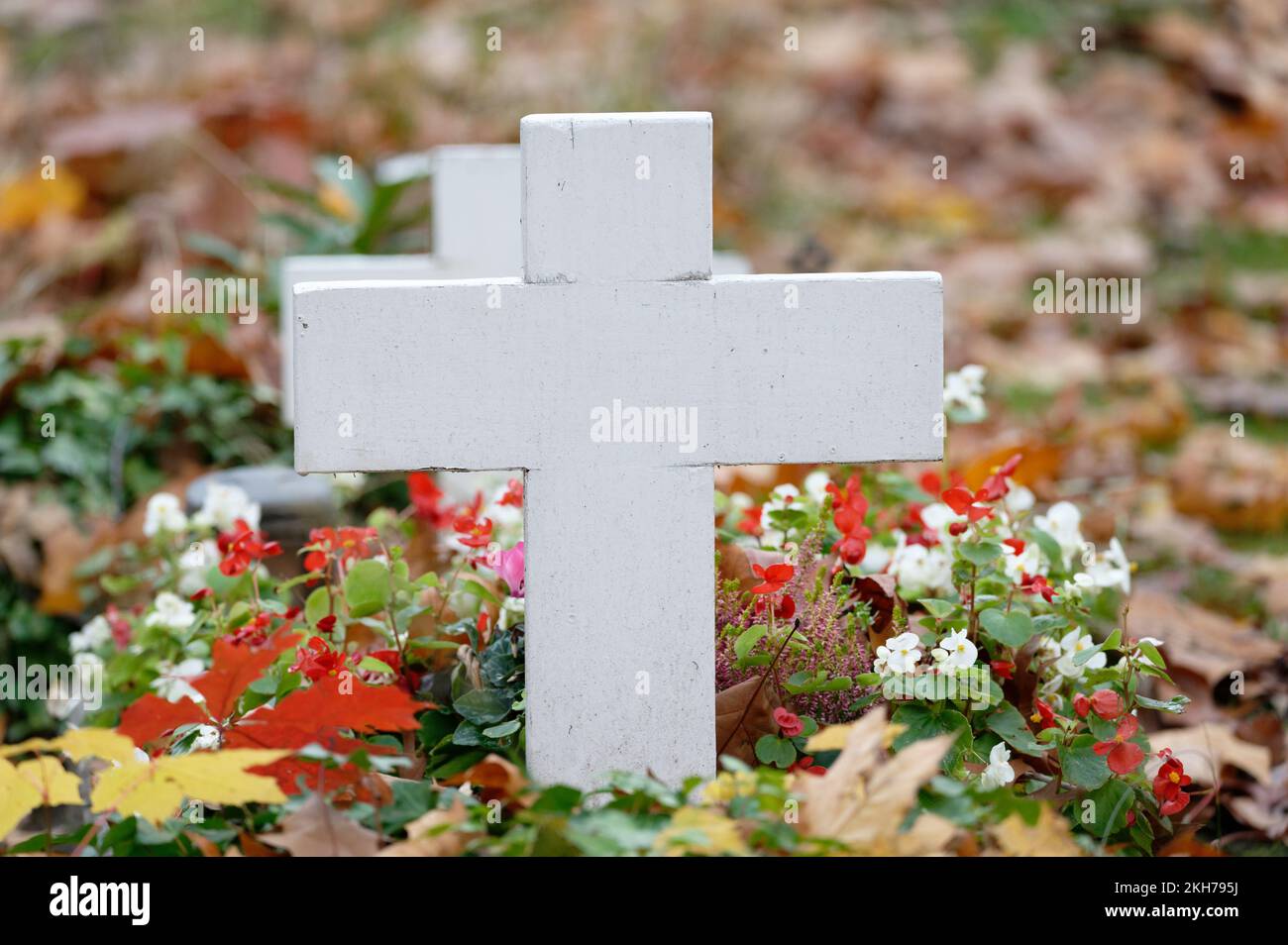 Weißes Kreuz eines Kindergrabes mit Blumen und Herbstblättern Stockfoto