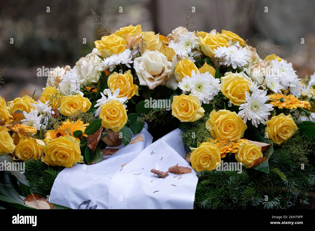 Grabblumen mit gelben Rosen und weißer Trauerschleife auf einem Grab mit herabfallenden Herbstblättern Stockfoto