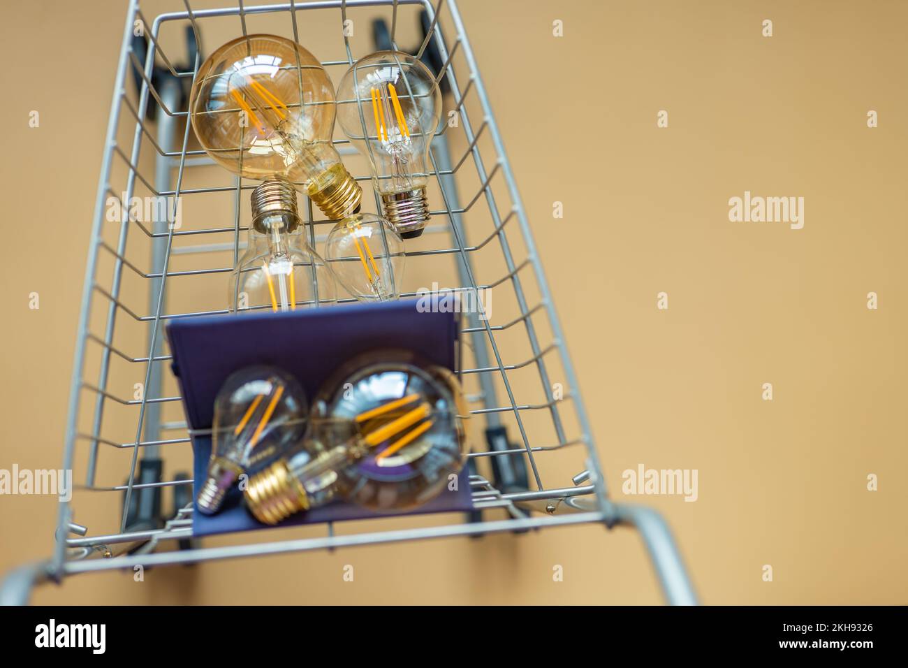 Verbrauch und Bezahlung des Energieverbrauchs. Glühbirnen in einem Supermarkt-Trolley auf beigem Hintergrund. Kauf von Strom. Viele Lampen in einem Stockfoto